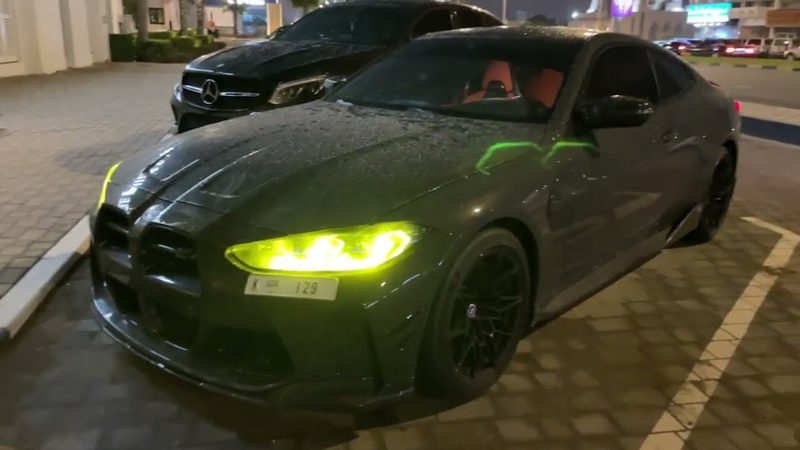A 2021 BMW M4 Competition parked at night with its headlights on.