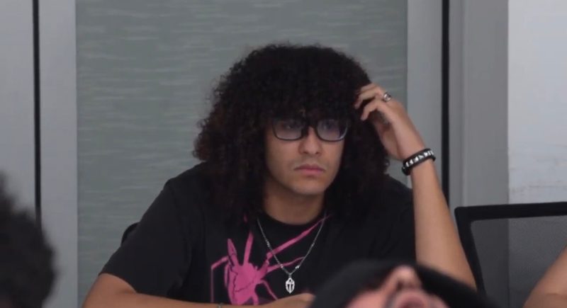 Still from the short film: a young man with curly hair and glasses, one hand on his head.